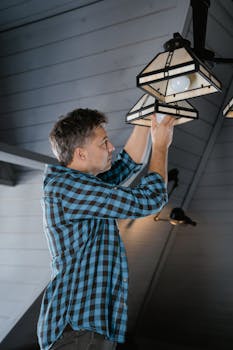 Adult man changing bulb in pendant light fixture, modern home interior setup.